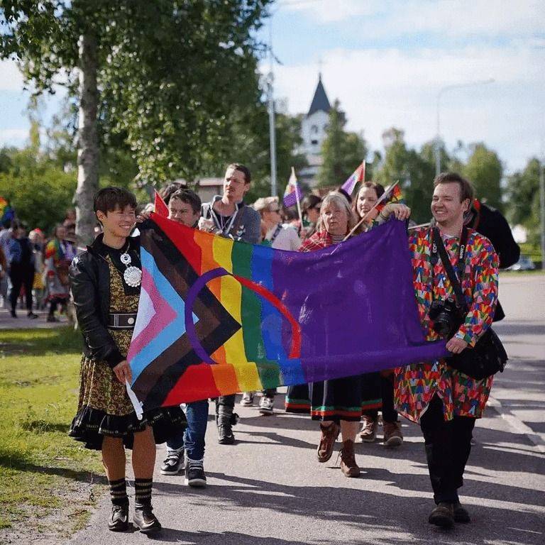 Front view of the Sápmi Pride parade, with two people holding a large Sápmi Pride flag in the front.