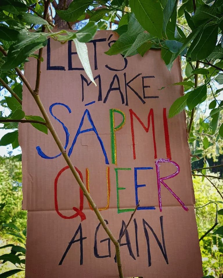 A cardboard sign in the woods saying "Let's make Sápmi queer again"