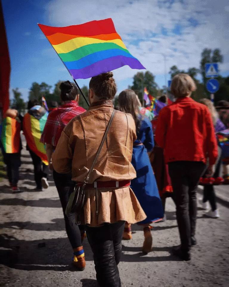 Back view of a person wearing Gákti, holding a Pride flag.